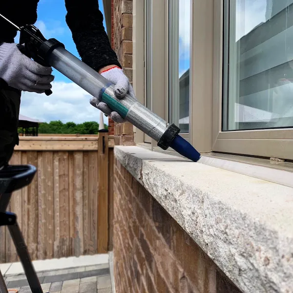 Worker caulking a window using a step ladder