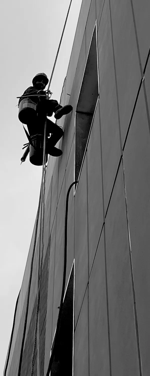 Worker caulking a window using a Bosun's chair